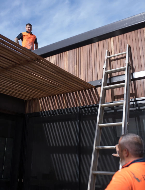 ladder leaning against building, one man on roof talking to another man on the ground